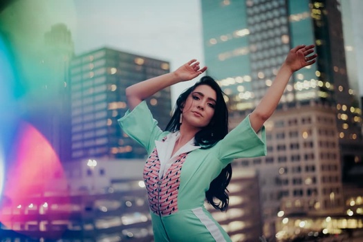 a vintage-style photo of a woman with her arms in the air, buildings behind her