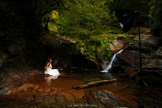 This is strobist photography. A speedlite in a softbox on location, with a model in a small pool next to a waterfall. It is like a studio on location.