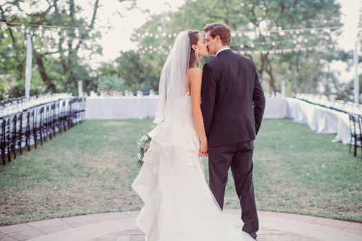 a wedding couple stands kissing in front of empty seats.