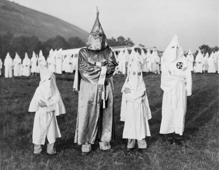 Children wearing Ku Klux Klan robes and hoods stand on either side of Dr. Samuel Green, a Ku Klux Klan Grand Dragon Children wearing Ku Klux Klan robes and hoods stand on either side of Dr. Samuel Green, a Ku Klux Klan Grand Dragon