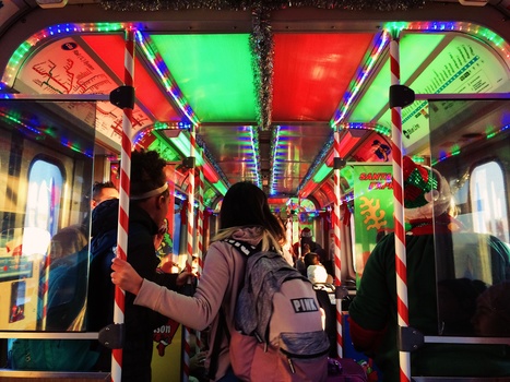 Person with backpack inside a neon-lit train car with vibrant red, green, and blue lighting panels overhead.