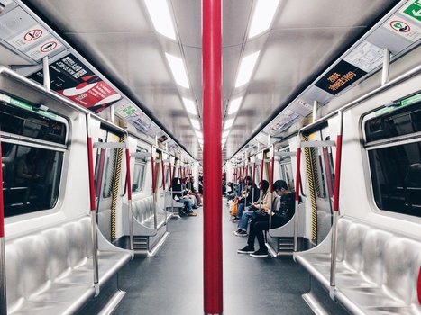 Interior of a subway train car with symmetrical perspective down the center aisle, red support pole dividing the frame.