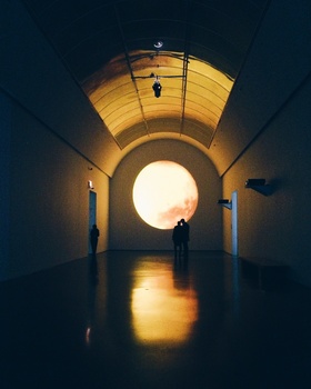 Silhouetted figure standing in a symmetrical tunnel with a bright circular opening at the center.
