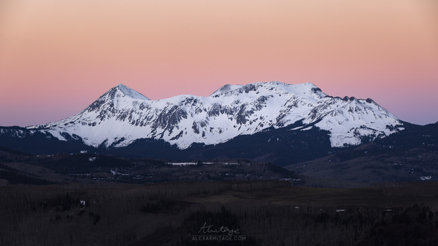 Snow-covered mountain peaks glowing pink under twilight sky at dusk.