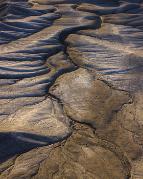 Aerial view of mudflats with intricate patterns of cracks and ridges creating geometric divisions across brown and tan terrain.