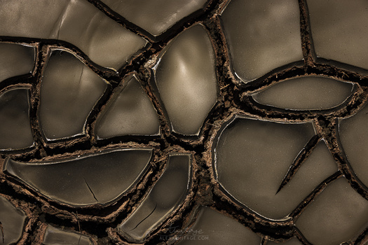 Close-up of dried, cracked mud with deep fissures creating organic geometric patterns against a neutral background.