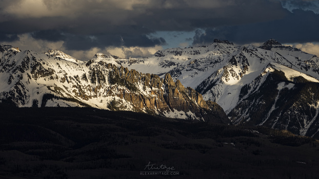 Snow-covered mountain range with dramatic cloud formations and golden sunlight illuminating the peaks.