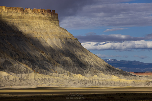 Dramatic desert mountain with layered geological formations and flat plain beneath golden afternoon light.