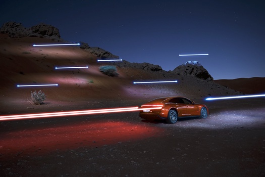 Orange sports car illuminated at night with light trails across a desert landscape.