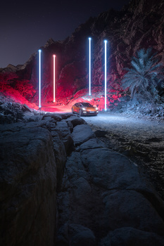 Neon light installation with vertical red and blue tubes illuminating a rocky landscape at night.