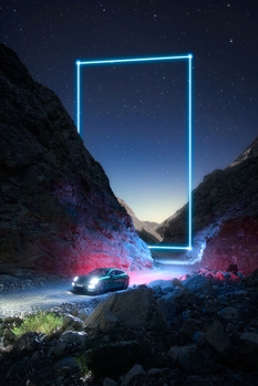 Sports car parked beneath a glowing blue neon rectangle frame suspended between dark canyon rocks at night.