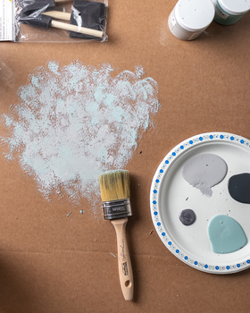 Paintbrush with white paint swatch on kraft paper next to palette of paint colors.