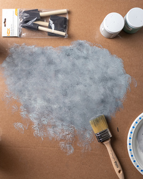 Overhead view of a wet concrete texture sample with paint supplies and brushes on brown paper.