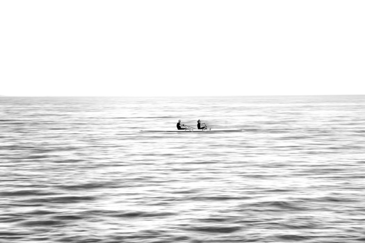 Two people in a small boat on calm, rippling water under an overcast sky.