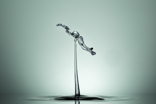 Water droplet frozen mid-splash against a gray background, forming a crown-like shape with extended tendrils.