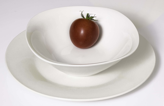 Brown tomato centered on a white ceramic bowl, stacked on matching plates against a plain background.