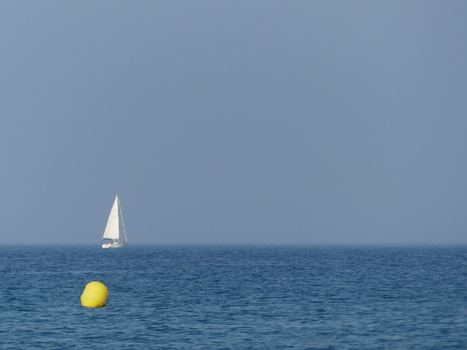 Sailboat with white sail on blue water with yellow buoy in foreground.