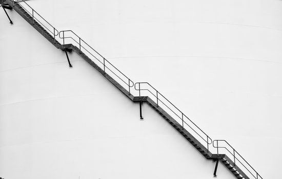 Metal staircase with handrails descending diagonally across a white wall.