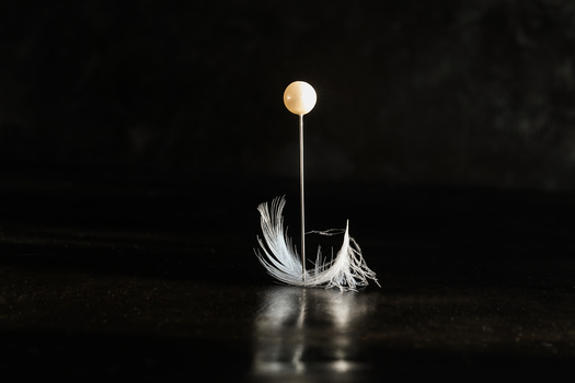 Feather suspended beneath a glowing orb on a thin wire against a dark background.