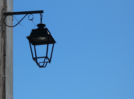 Silhouetted traditional lantern hanging from ornate bracket against clear blue sky.
