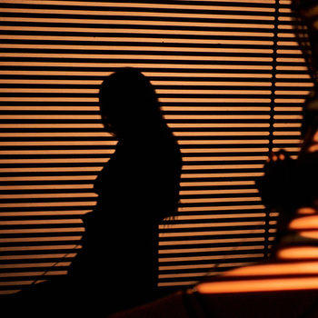 Silhouette of a seated figure against a striped orange and black background with dramatic side lighting.