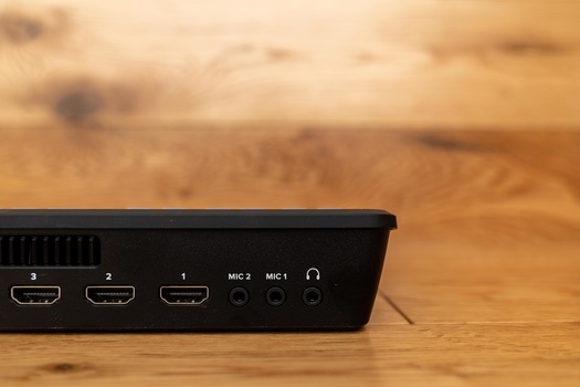Black audio/video interface device with three HDMI ports and two microphone inputs on wooden surface.