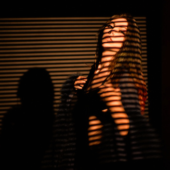 Silhouetted figure with horizontal light stripes casting dramatic shadows across body and wall.