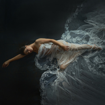 Woman in sheer dress suspended horizontally against dark background with billowing fabric.