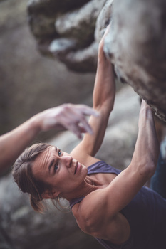 Rock climber gripping an overhang on an outdoor climbing wall, shot from below with natural lighting.