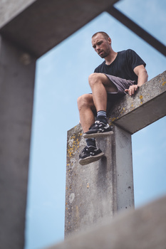 Man sitting on concrete ledge against blue sky, shot from low angle perspective.