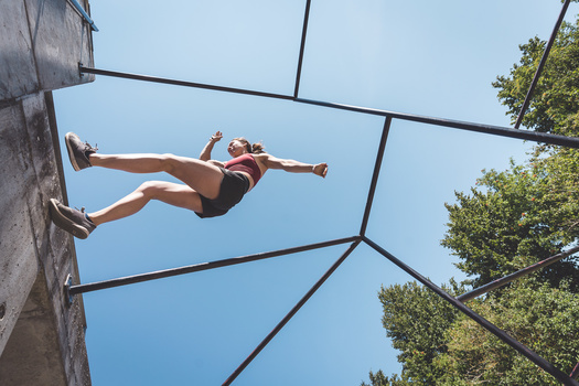 Athlete suspended horizontally in mid-air on an obstacle course structure against blue sky.