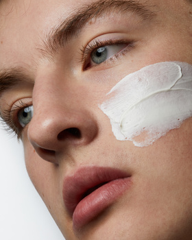 Close-up portrait of a person's face with a white cream or skincare product applied to one cheek.