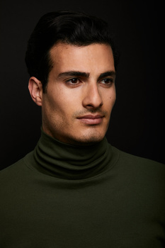 Man wearing olive turtleneck against dark background, studio portrait lighting.