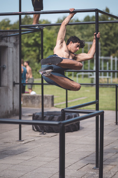 Athlete performing a dynamic pull-up movement on an outdoor bar with legs extended in mid-air.