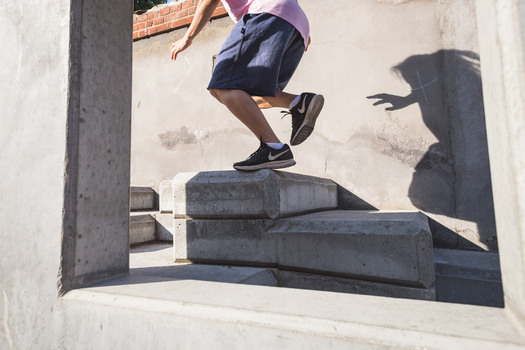 Athlete mid-jump over concrete blocks casting sharp shadows on white wall.