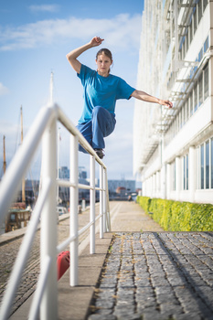 Skateboarder performing a trick over a metal handrail on a paved urban plaza.