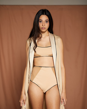 Woman in beige cardigan and coordinating two-piece swimwear against warm tan backdrop.