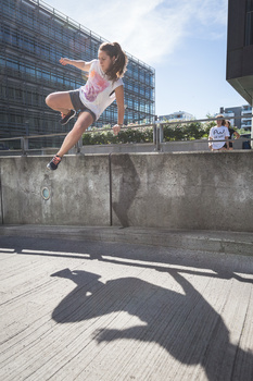 Parkour athlete jumping over a concrete barrier with urban buildings in background.