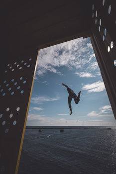 Person diving from a ship's railing into blue ocean water below.