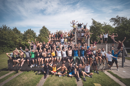 Large group of young people posed on tiered outdoor structure with arms raised in celebration.
