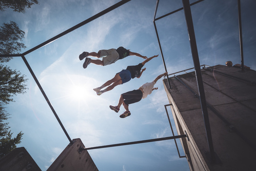 Three people jumping on a trampoline photographed from below against a bright sky.