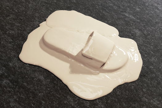 White cosmetic product sample on dark textured surface with organic pooling effect.