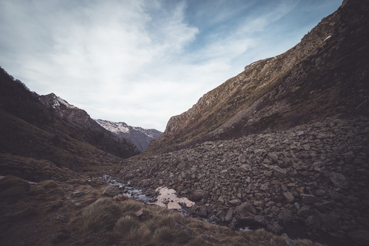 Mountain valley with a small stream flowing between rocky slopes under partly cloudy skies.