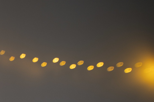 String of out-of-focus warm yellow lights against a dark gray sky, creating bokeh orbs in a diagonal line.