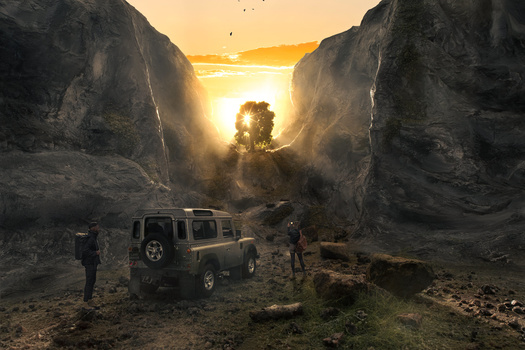 Off-road vehicle parked in a dramatic canyon with golden sunset light streaming between towering rock walls.