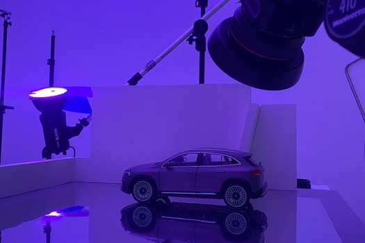 SUV model car on reflective surface under purple studio lighting with professional equipment visible.