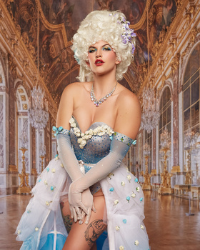 Portrait of a woman with white voluminous hair and bold red lips posed in an ornate golden interior.