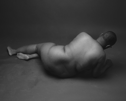 Nude male figure lying on his side against a neutral background in black and white.