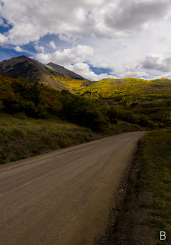 Unpaved dirt road stretching toward distant mountains under partly cloudy sky.