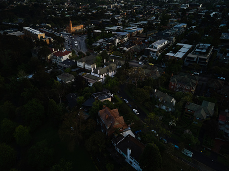 Aerial nighttime view of a residential neighborhood with illuminated buildings surrounded by dark trees.